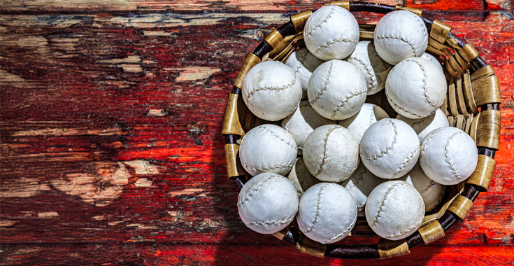 Basket filled with white cricket balls on a weathered red wooden surface.